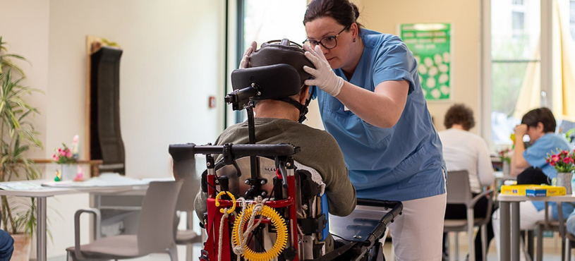 Eine Pflegerin auf Station 5 (für komplexe Behinderungen) der Fachklinik für Neurologie im Epilepsiezentrum Kleinwachau in Radeberg bei Dresden hilft einem Epilepsie-Patienten mit dem Anlegen seines Kopfschutzes. 
