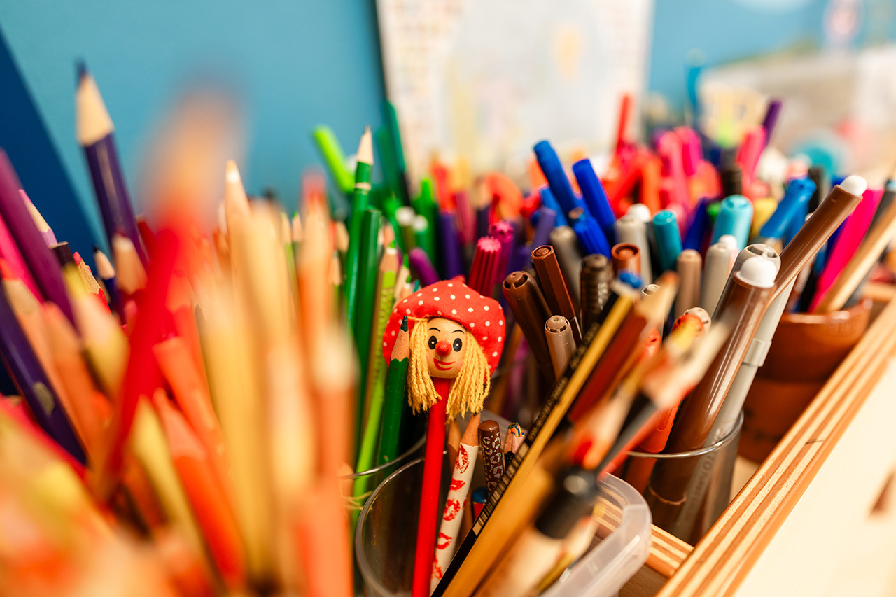 viele bunte Stifte, bei einem ist ein Gesicht zu erkennen